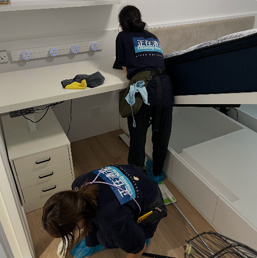 Two people in cleaning uniforms working on a bed in a room.